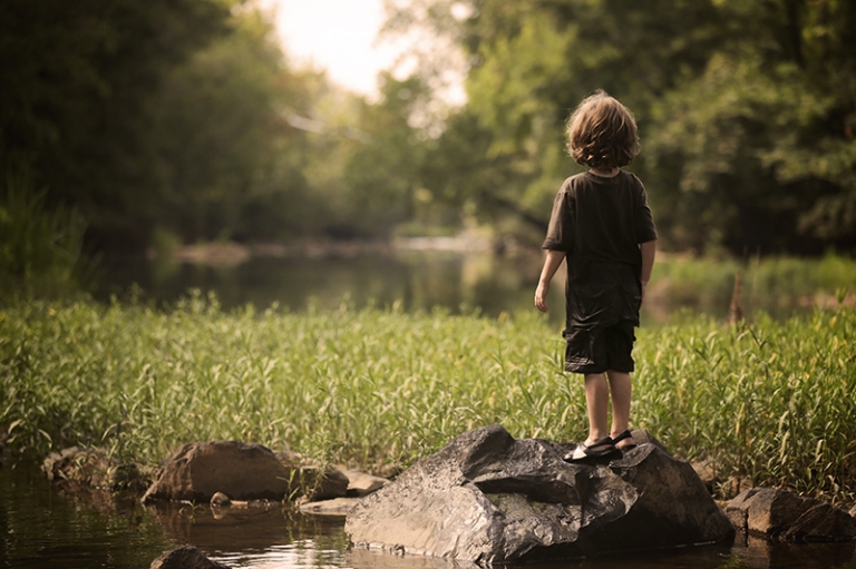 A little boy standing on a rock and looking out over the water