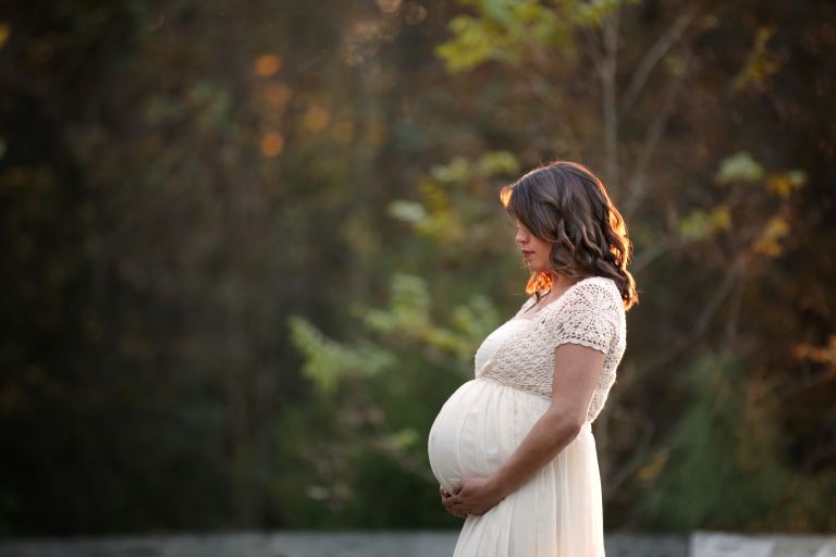 Beautiful woman 8 months pregnant, holding her tummy. The light is coming through her hair as she is being back lit. 