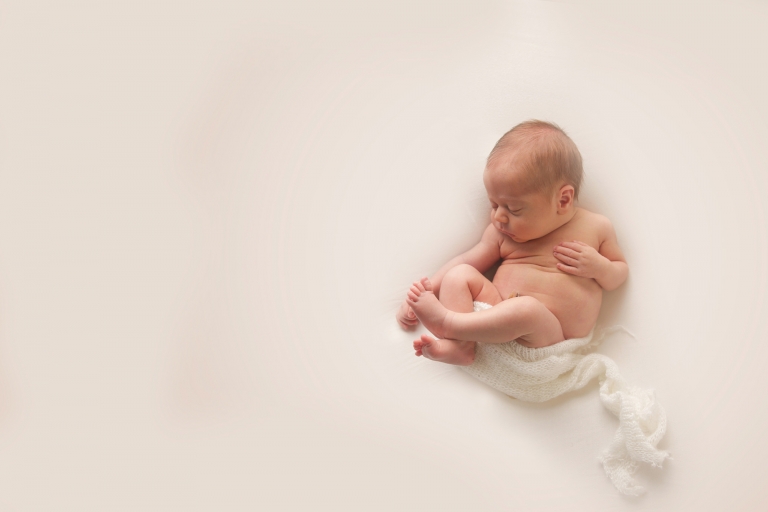 beautiful newborn baby laying naked with a white wrap lightly covering her on a white background