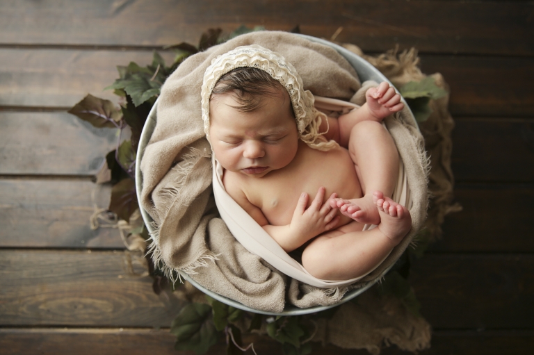 newborn in a basket with a wreath of leaves around them. This is a prop shot