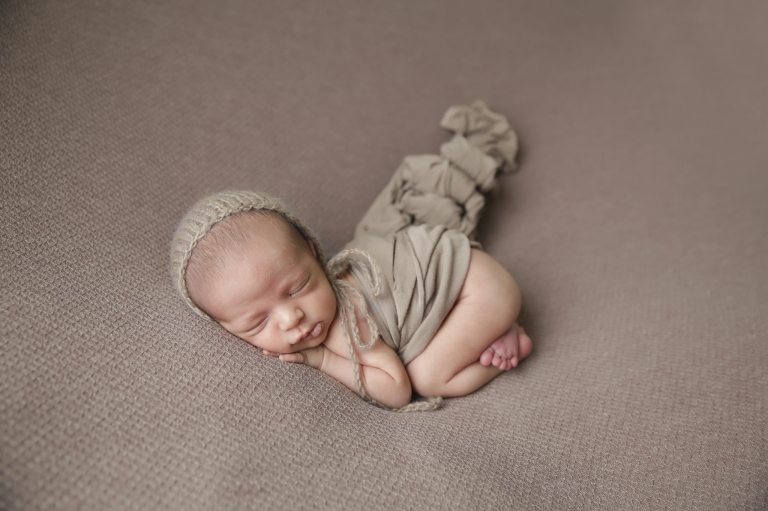 tiny newborn in sleepy pose on beige background