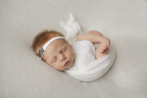 Newborn baby safely wrapped in white wrap with matching headband and snuggled up