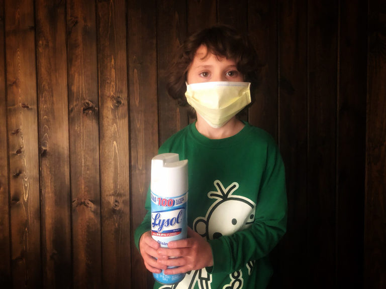 Little boy in the studio wearing a face mask and holding a bottle of lysol.  In prevention of the coronavirus